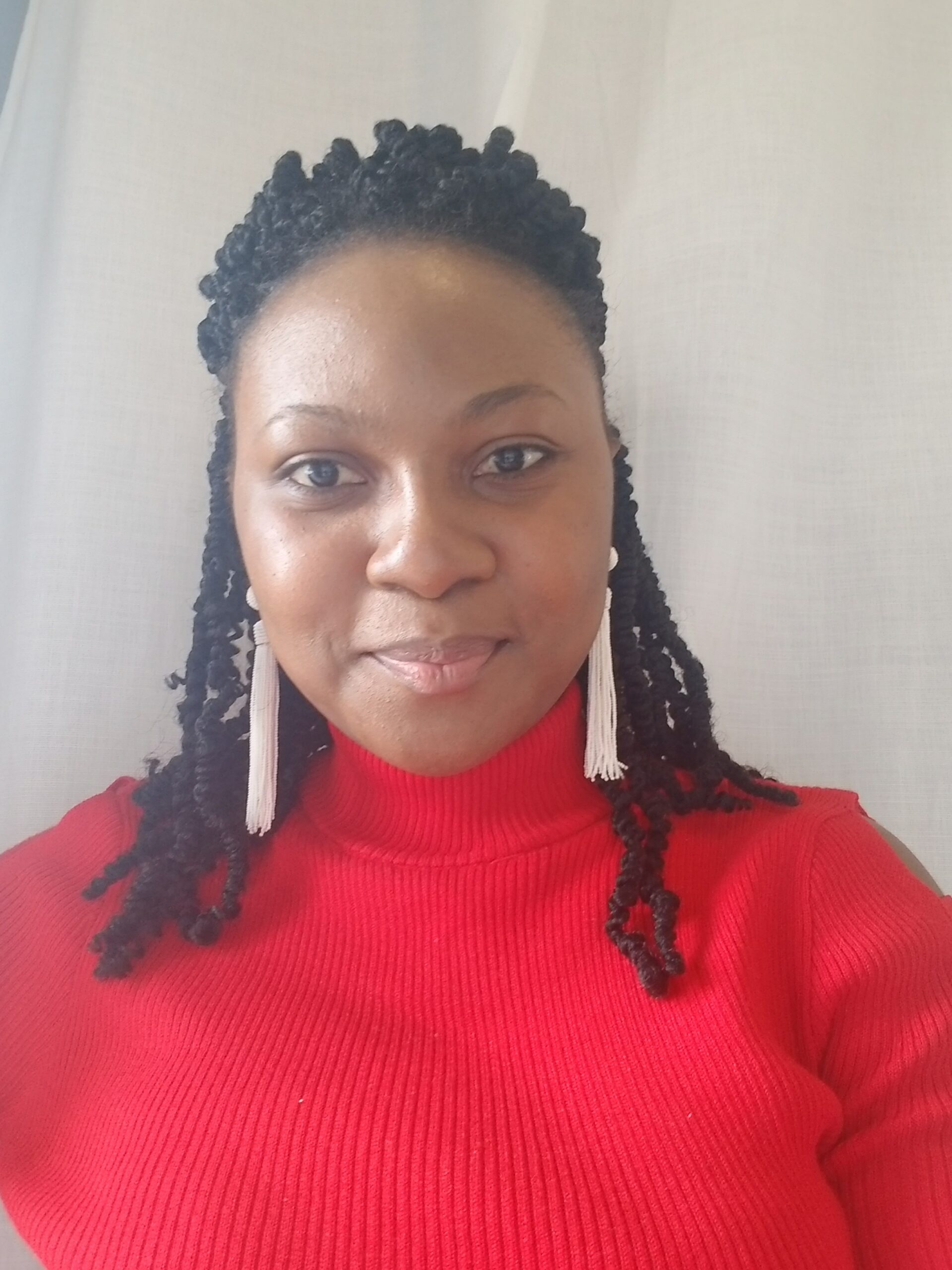 Picture of young black girl smiling into camera with braids, shiny dangling earrings and a red turtleneck.